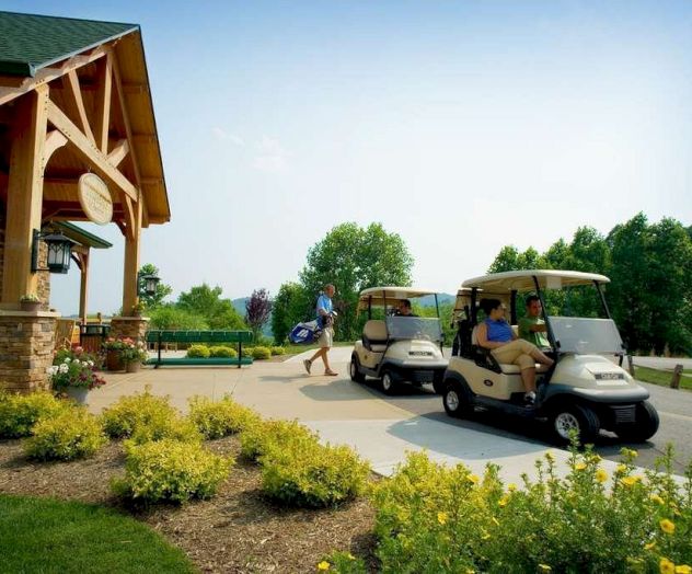 Two golf carts are parked near a building with people nearby, surrounded by greenery and neatly trimmed shrubs.
