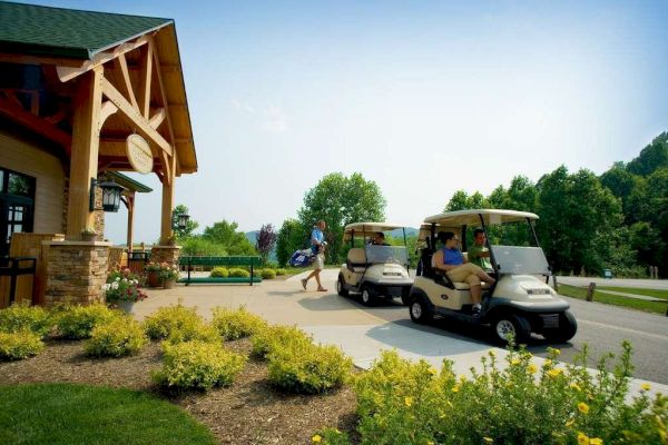 People near golf carts outside a building with plants and trees around.
