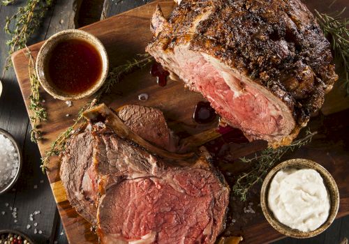 A platter with sliced roast beef, gravy, horseradish sauce, and mashed potatoes, garnished with herbs and served with asparagus.