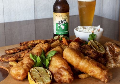 A meal with fried fish, lemon, fries, coleslaw, parsley garnish, a beer bottle, and a filled beer glass on a table setting.