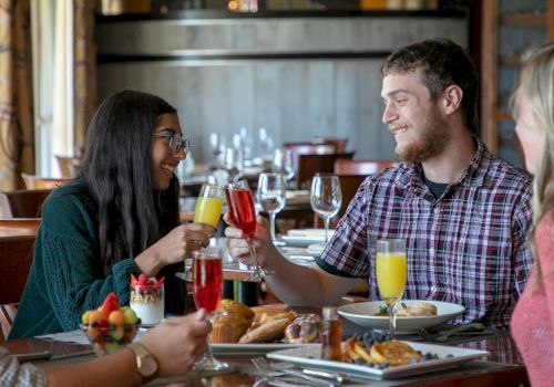 People sitting at a table in a restaurant, enjoying food and drinks, while smiling and toasting with glasses.