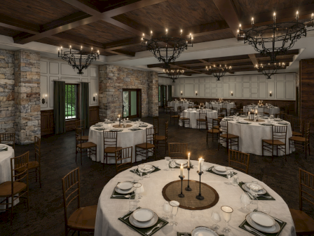 A rustic, elegant banquet hall with round tables, white linens, modern candles, stone and wood walls, and chandeliers under a coffered ceiling.