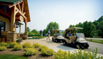 People near golf carts outside a building with landscaping and trees, preparing for a game.